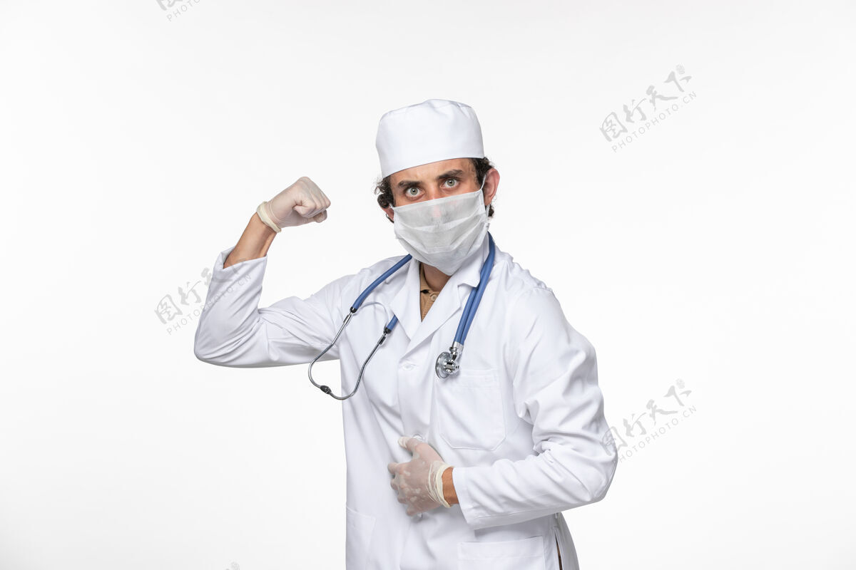 冠状病毒正面图：男医生穿着医疗服 戴着无菌口罩 以防白墙病毒引起的冠状病毒大流行对人体造成危害消毒前实验室外套