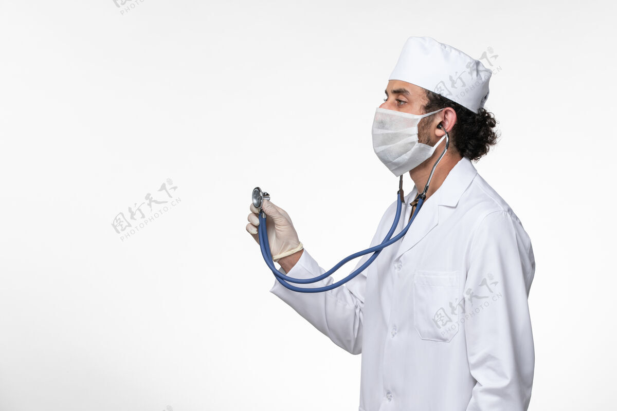 冠状病毒预防正面图：男医生穿着医疗服 戴着口罩以防病毒感染-使用听诊器对白墙病病毒进行病毒感染-大流行医生使用冠状病毒防护