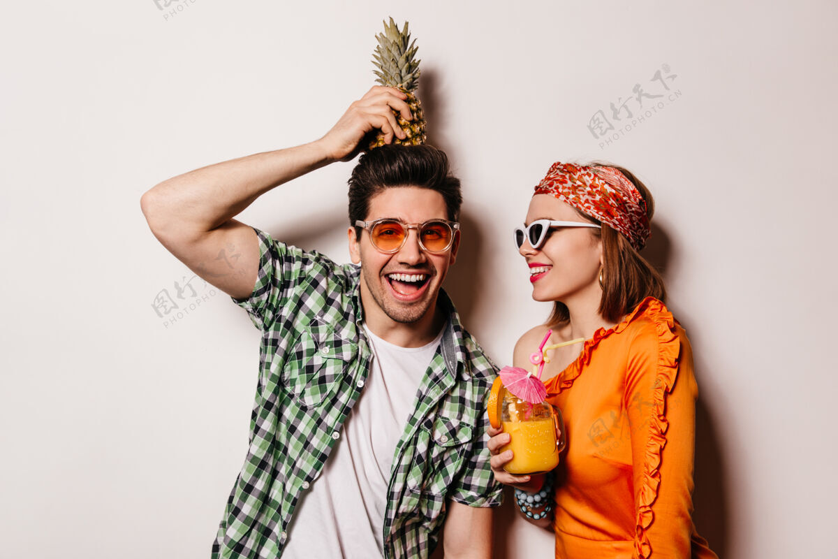 漂亮穿着绿色衬衫的淘气男人头上顶着菠萝 微笑着看着镜头穿着橙色衬衫戴着眼镜的女士手里拿着鸡尾酒金发女性手