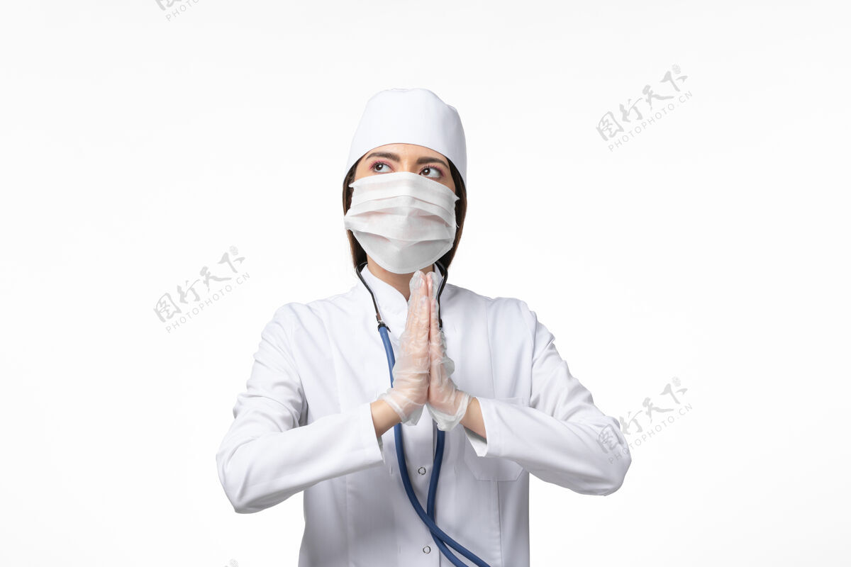 专业正面图女医生穿着白色无菌医疗服带口罩因冠状病毒祈祷白墙病大流行病毒covid-女性服务面罩