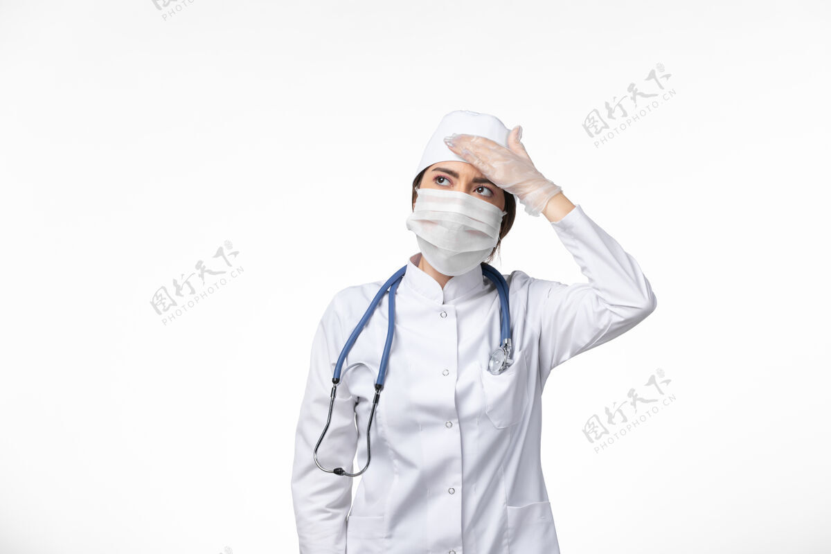 听诊器正面图：女医生身穿白色无菌医疗服 戴口罩 因柯维德-头痛白墙病病毒柯维德-大流行性疾病医生人面罩