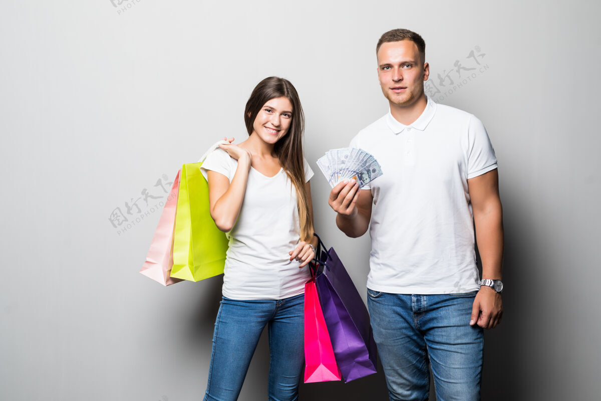 购物美丽的年轻微笑阳光学生夫妇举行了许多彩色购物袋隔离在白色背景欢呼手关系