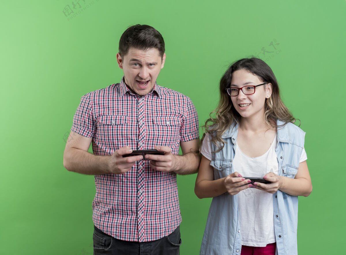 夫妇幸福的年轻夫妇在绿色的墙壁上微笑着站着使用小器具的男人和女人看站微笑