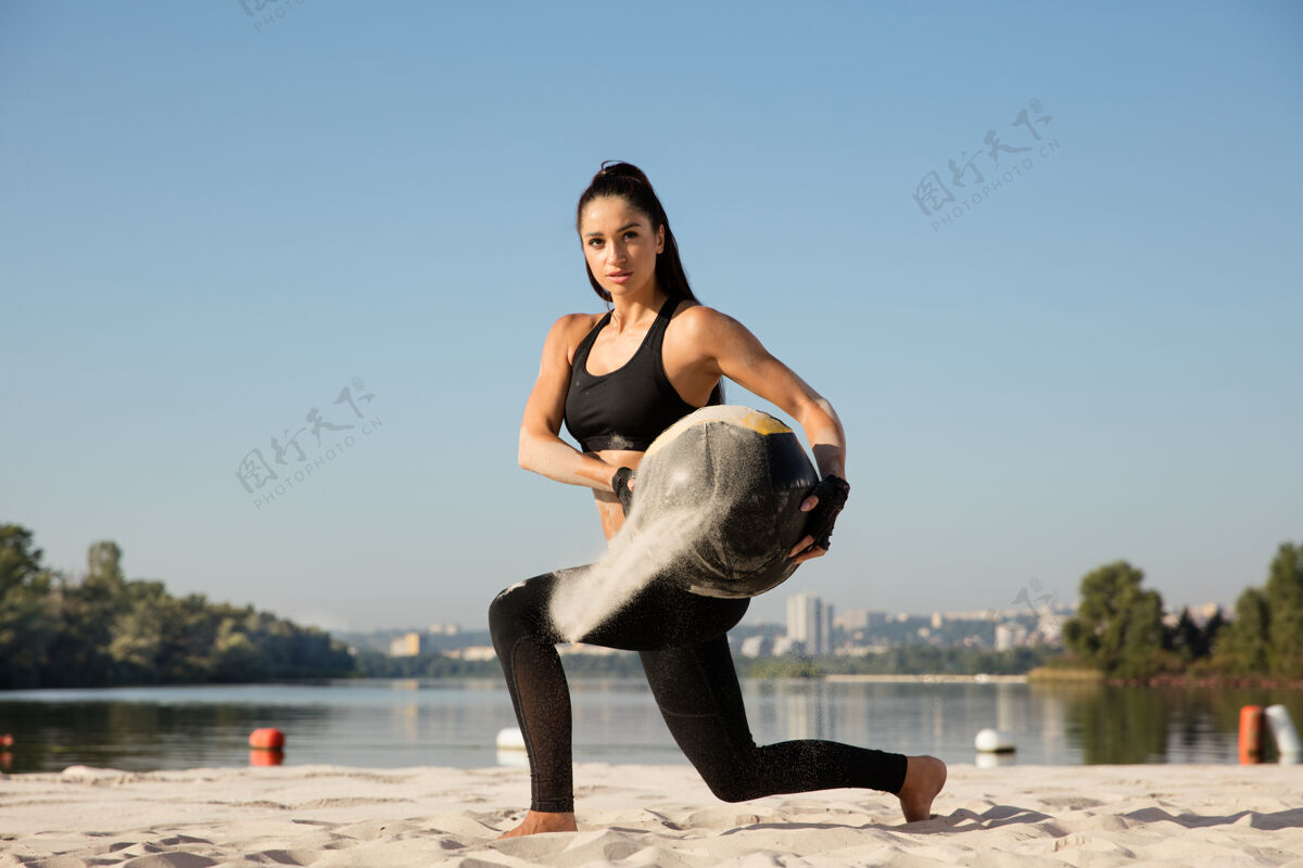 瘦年轻健康的女人在沙滩上带球做弓箭步力量运动空气