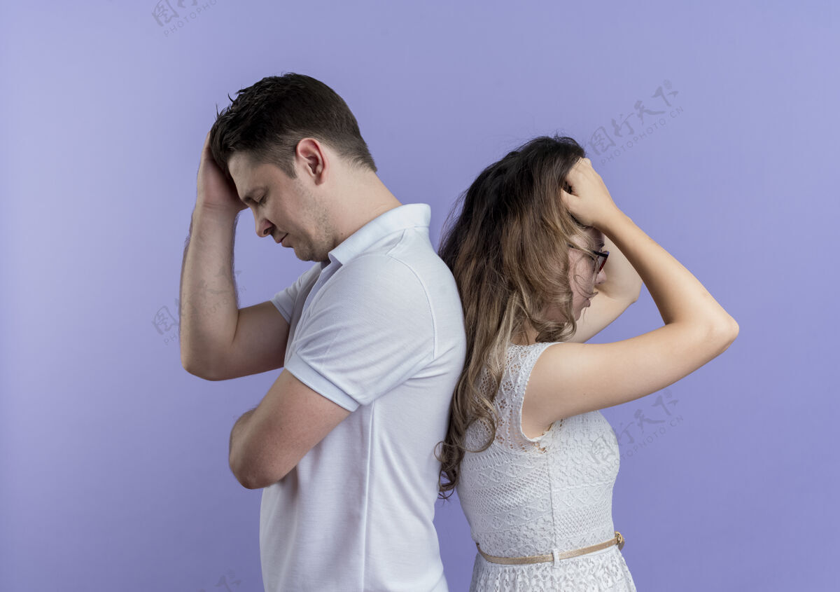 男人一对年轻夫妇背靠背地站在蓝色的墙壁上 心烦意乱女人心烦意乱夫妇