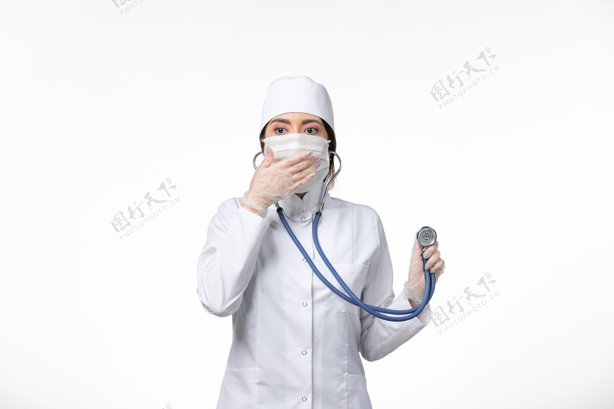 套装正面图女医生身穿白色无菌医疗服 戴口罩 因冠状病毒-使用听诊器对轻白墙病病毒冠状病毒-大流行性疾病病毒医疗大流行