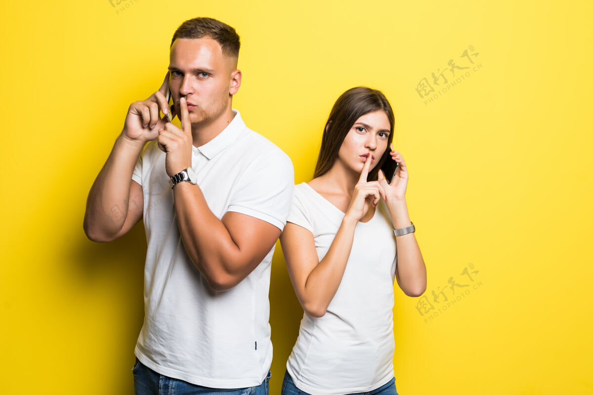 漂亮男人和女孩在用黄色隔离的手机交谈时请安静休闲看夫妻