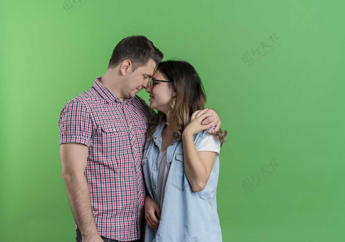 男人一对穿着休闲服的年轻男女站在一起 在绿色的墙上拥抱着幸福的爱情拥抱站着衣服