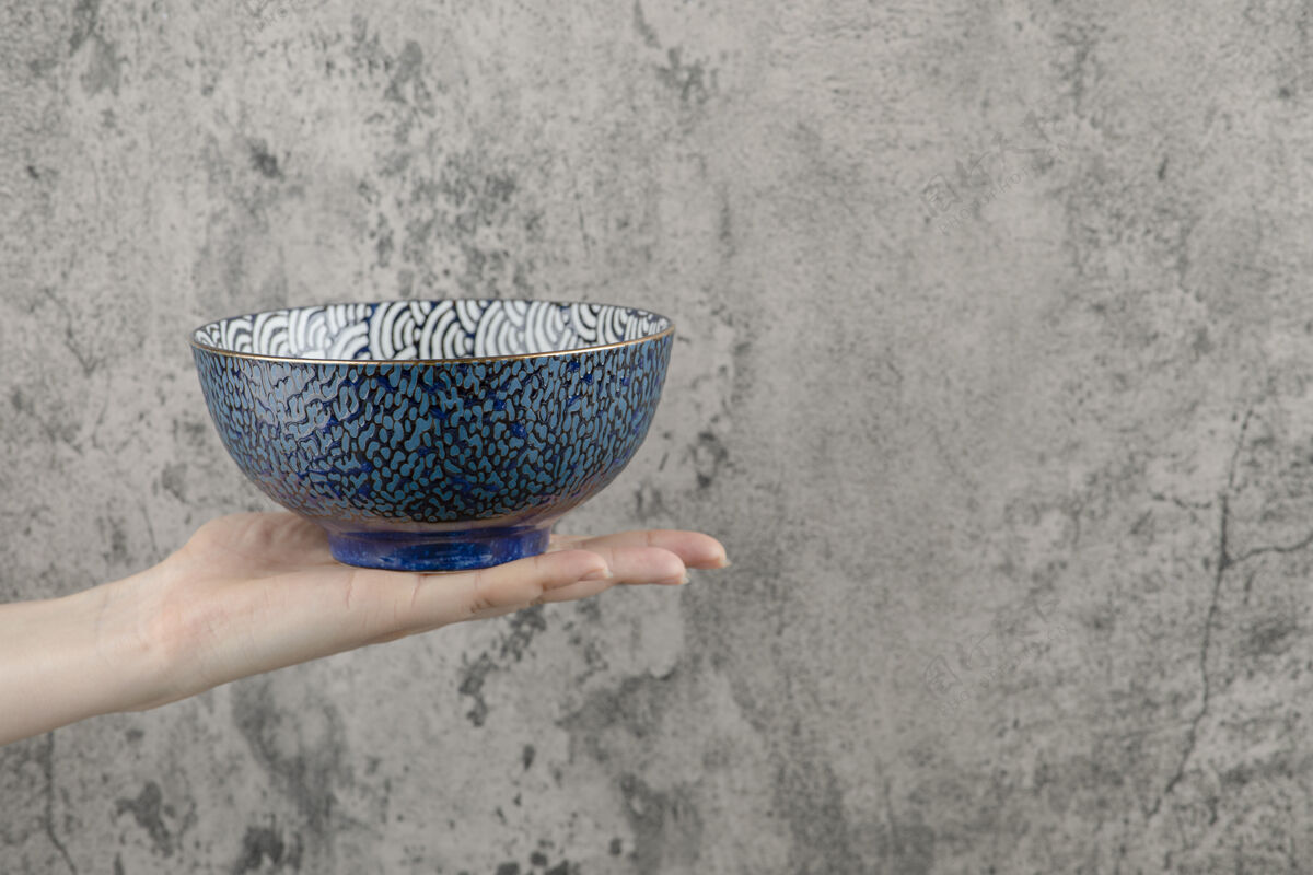厨具女性手拿着大理石背景上的空蓝碗餐具容器陶瓷