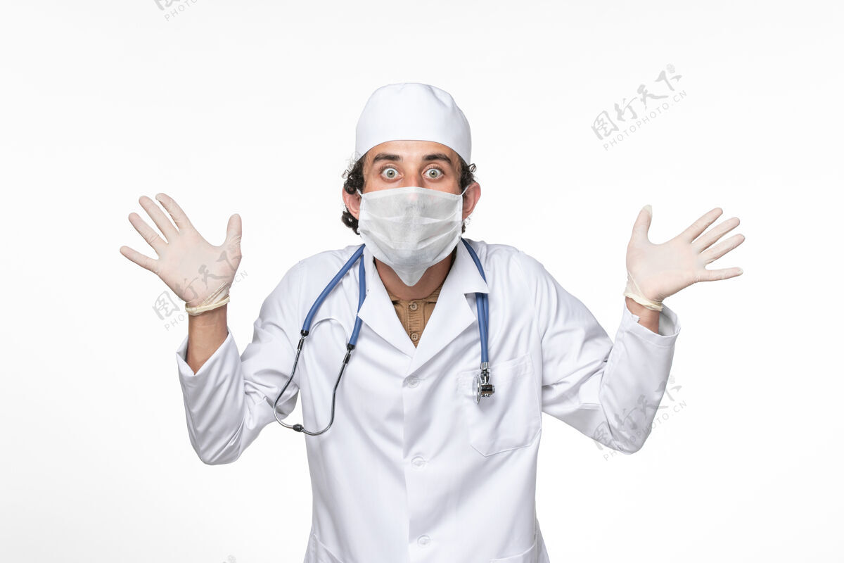 专业正面图身穿医疗服的男医生戴着无菌口罩 以防白色桌面上的冠状病毒溅起病毒大流行男性人医疗