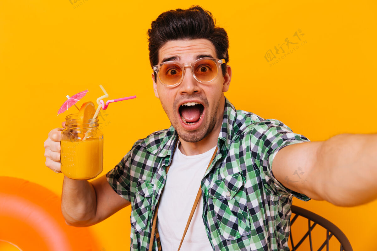 衣服一个戴着墨镜 穿着绿衬衫的男人自拍了一张照片 惊讶地看着相机照片上是一个在孤立的空间里拿着一杯鸡尾酒的家伙充气圈休闲鸡尾酒