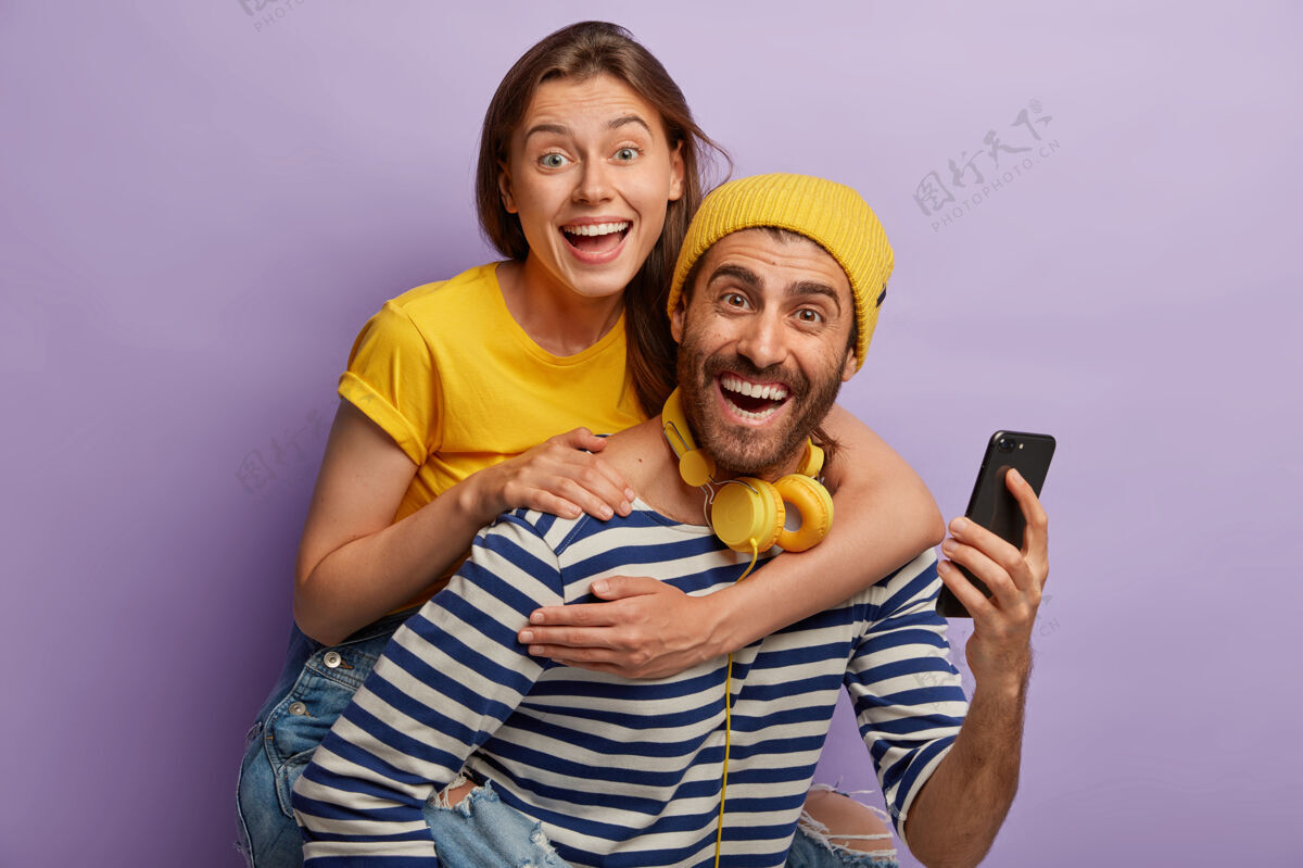 骑马年轻男女朋友在一起玩的照片 男人背着女人 用手机 欢笑 隔着紫色的墙快乐的博客朋友男性用户