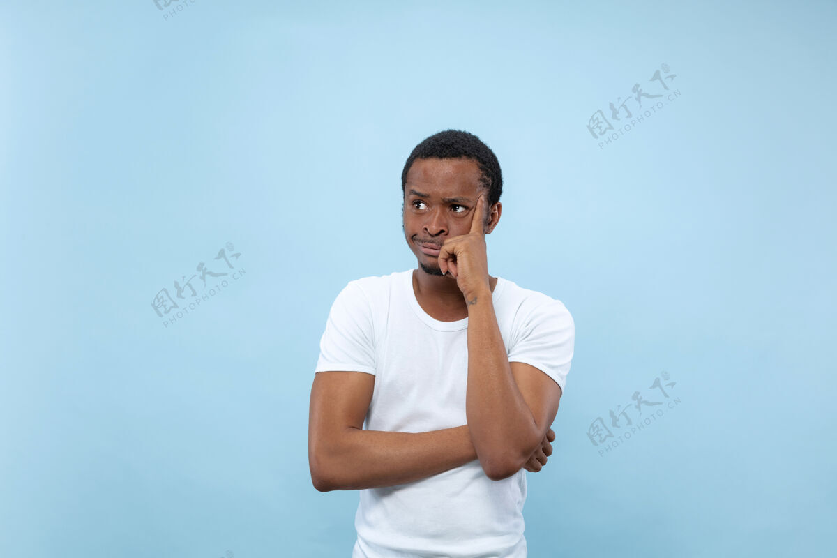 工作半身特写肖像的年轻非洲裔美国男子在白色衬衫的蓝色空间人类的情感 面部表情 广告概念人类选择思想