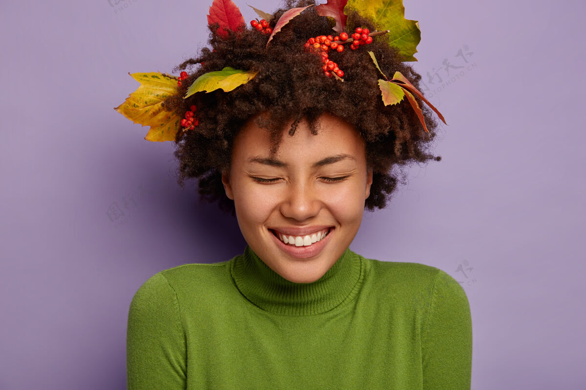 绿色可爱的非裔美国女人的特写肖像笑得很大声 有宽阔的牙齿微笑 闭上眼睛不高兴 戴着秋叶扎在头发上心情很好紫色卷发高兴