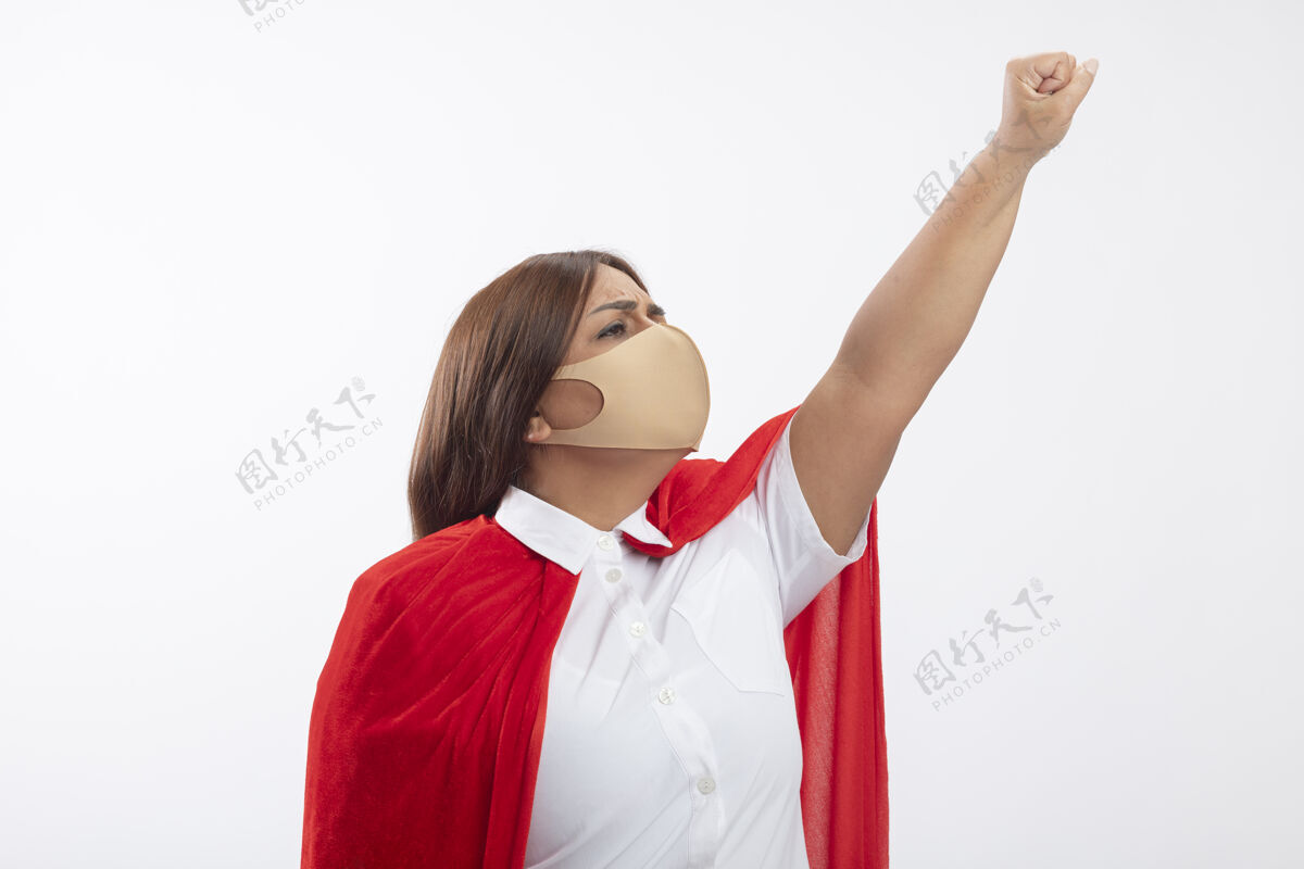 白色自信的中年女超人戴着医用口罩看着侧举拳头孤立在白色穿提高看