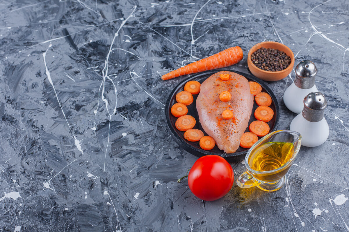 胸脯把鸡胸肉和胡萝卜片放在盘子里 在蓝色的表面放上盐 油 香料 胡萝卜和西红柿碗有机蛋白质