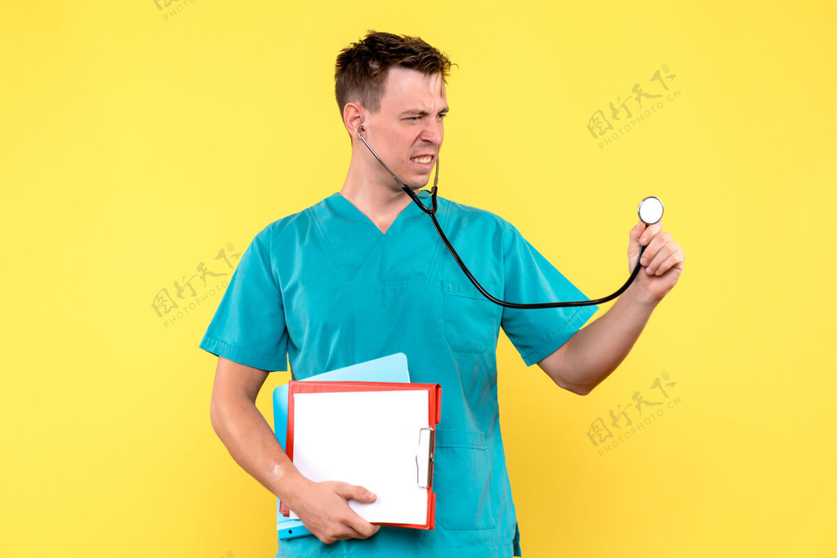 人黄墙上年轻男医生拿着文件的正视图医院年轻的男医生微笑