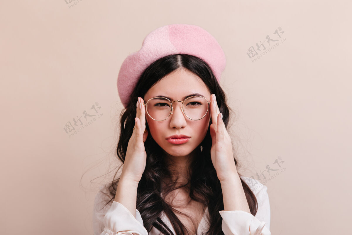 有趣戴着眼镜的沉思的中国女人看着相机戴着贝雷帽的滑稽亚洲模特在米色背景下摆姿势法式风格性感年轻