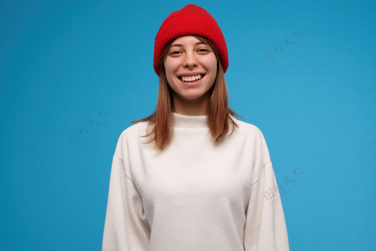 20多岁十几岁的女孩 快乐的女人 深色头发 穿着白毛衣 戴着红帽子 笑容灿烂 人的概念 隔着蓝色的墙女孩黑发休闲