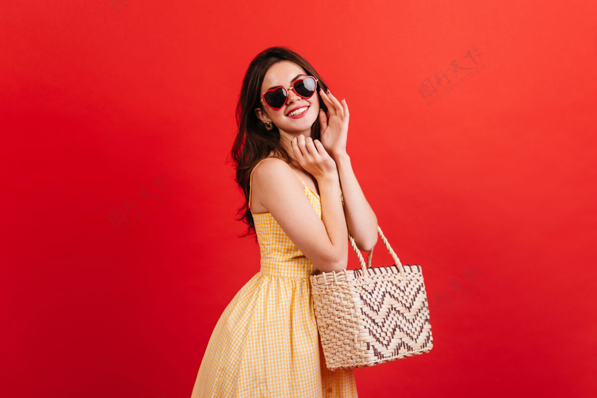 休闲积极的女人在红墙上兴高采烈地摆姿势的肖像深色头发的女人穿着明亮的夏季服装拿着沙滩包女人完美自信