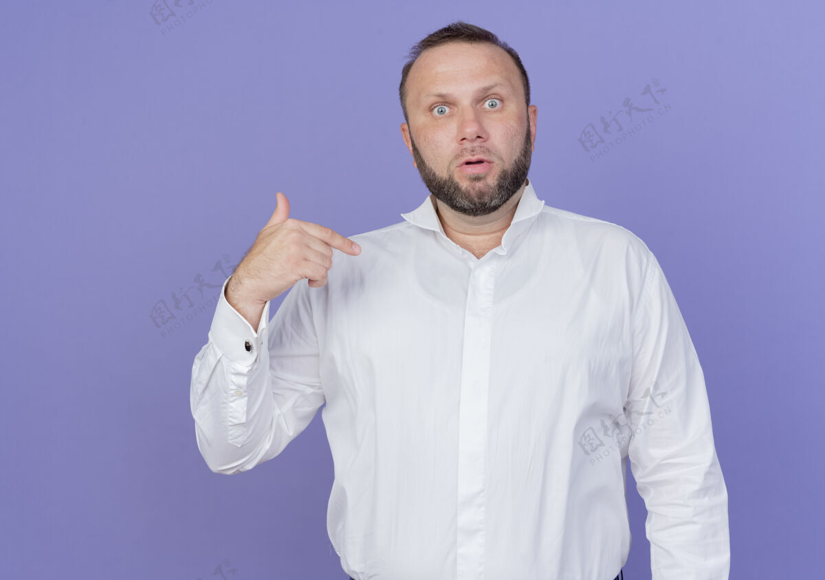 男人一个留着胡子的穿白衬衫的男人站在蓝色的墙上 看着自己困惑和惊讶胡子站他自己