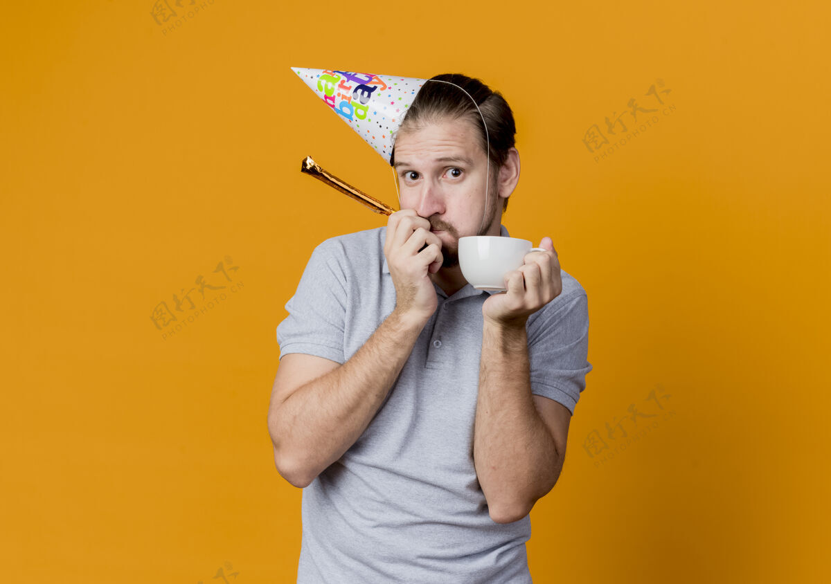 拿着戴着节日帽的年轻人举着咖啡帽庆祝生日站在橙色的墙上 看上去既惊讶又困惑男人惊喜庆祝