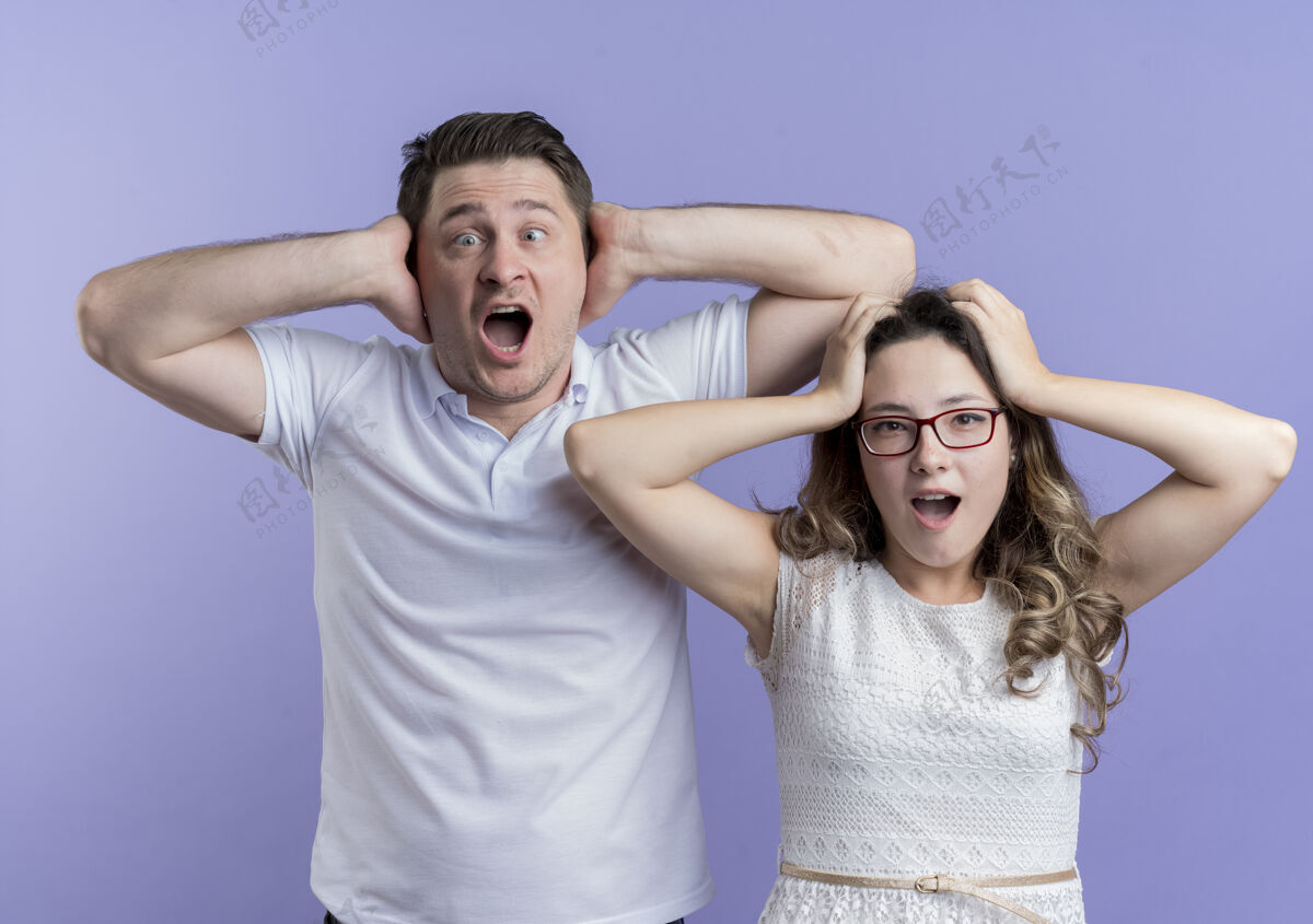 年轻一对年轻的夫妇看起来很困惑 非常焦急 他们站在蓝色的墙上用手抚摸着头触摸焦虑站