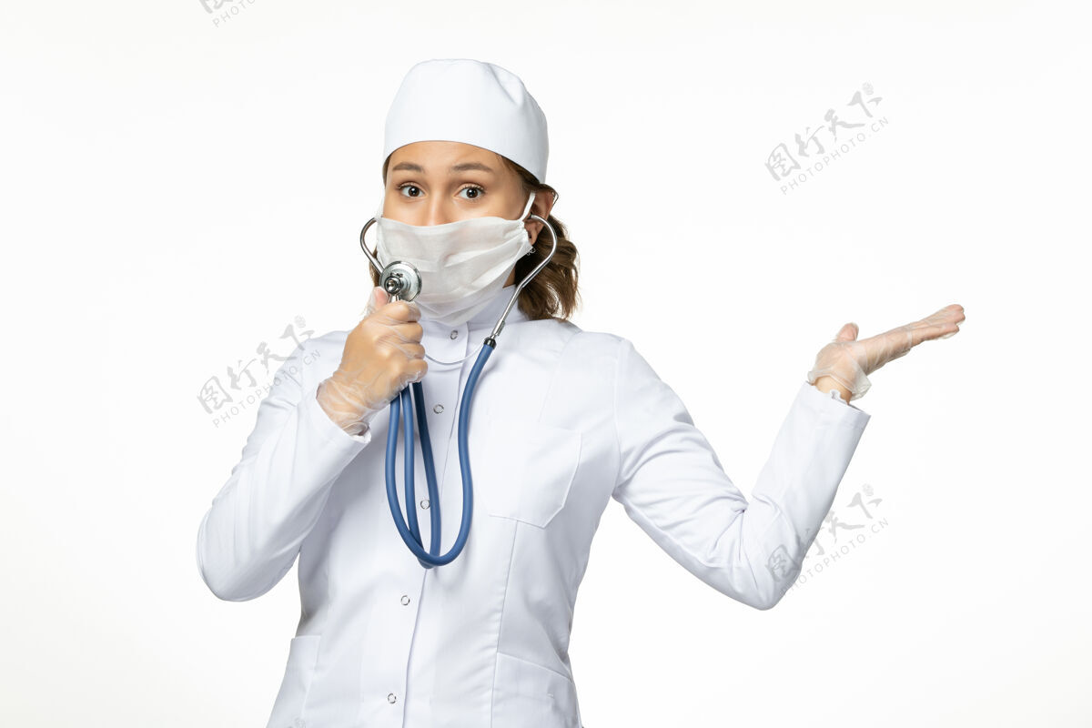 病毒正面图年轻女医生戴着防护性无菌口罩由于冠状病毒使用听诊器在白色办公桌上到期佩戴正面