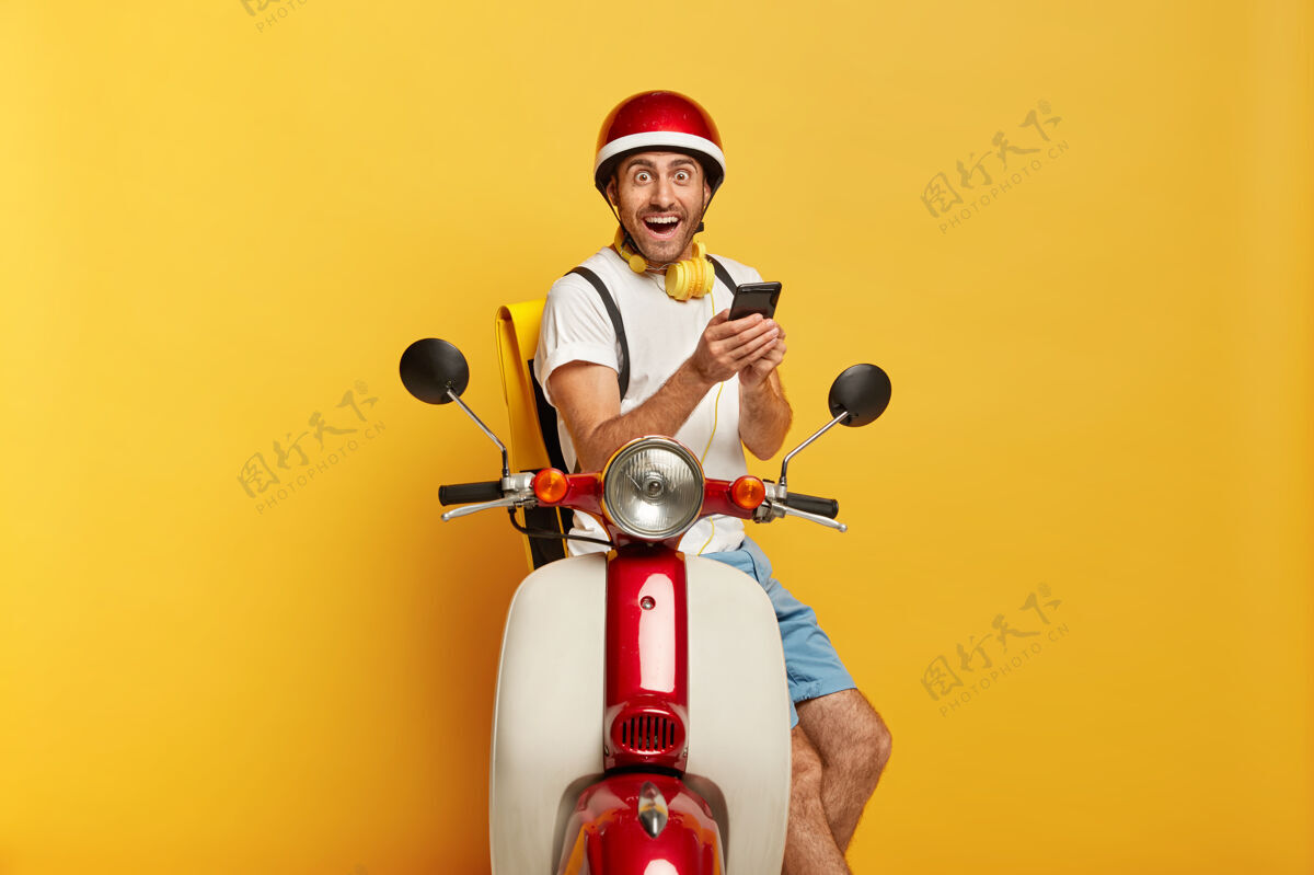 欢呼喜出望外的英俊男司机骑着红色头盔的滑板车的照片摩托车摩托车道路