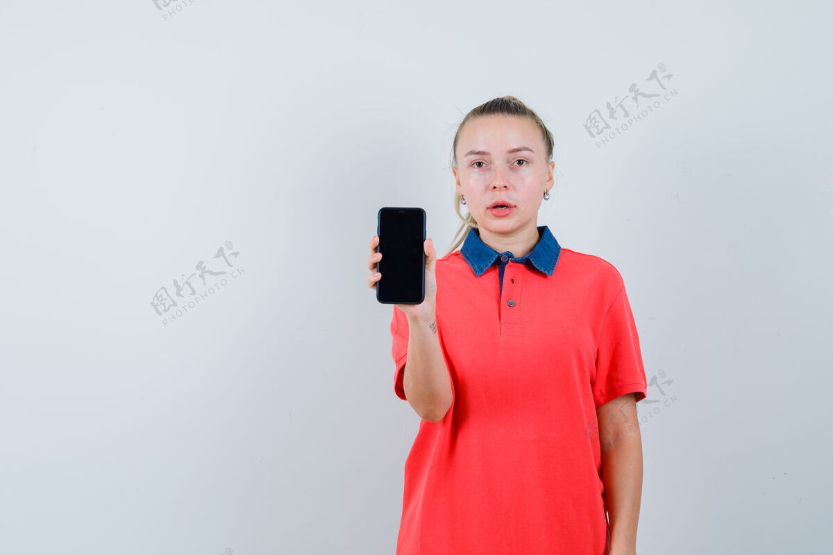 年轻一个穿着t恤展示手机的年轻女子 看上去很困惑外观休闲表演