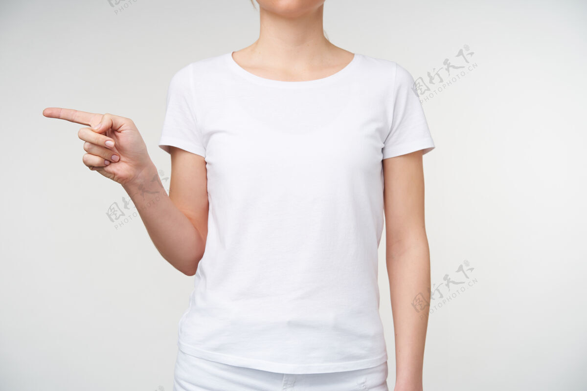 室内室内拍摄的年轻女性穿着基本白色t恤 食指指向一边 同时显示手语上的字母g 站在白色背景上手势符号身体