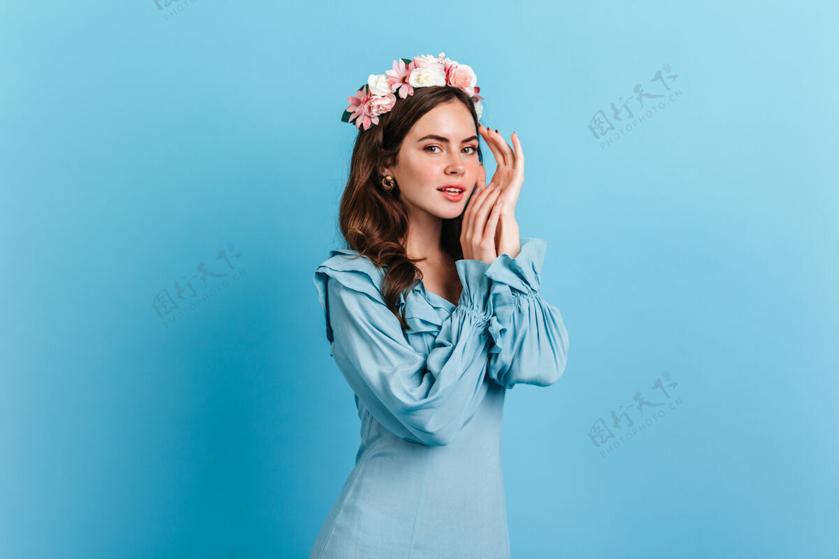 优雅迷人的女士穿着优雅的蓝色礼服在隔离墙上摆姿势室内的年轻女子肖像 粉红色的花 深色的头发模特可爱时尚