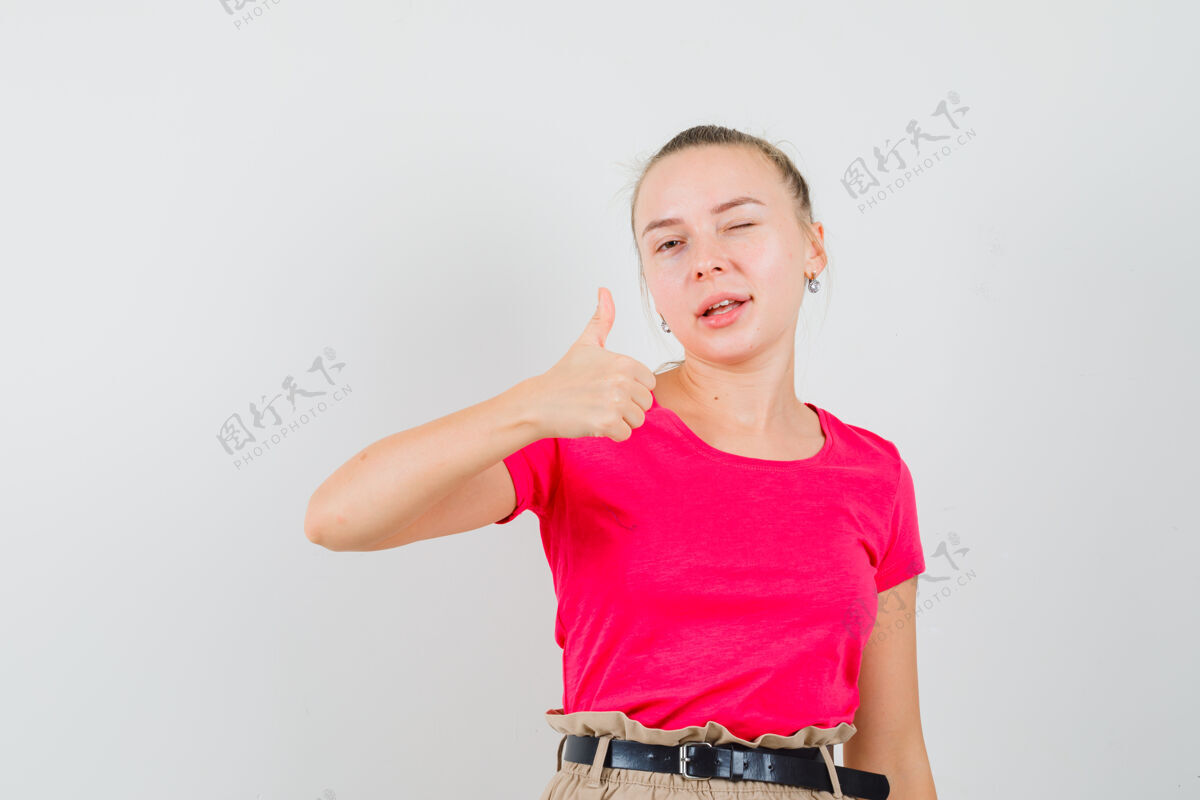 裤子年轻女子向上展示拇指 在t恤和裤子前视图眨眼年轻表演脸