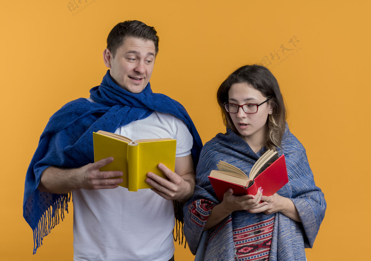 夫妻一对年轻夫妇拿着毯子拿着书幸福而积极地微笑着站在橙色的墙上毯子积极女人