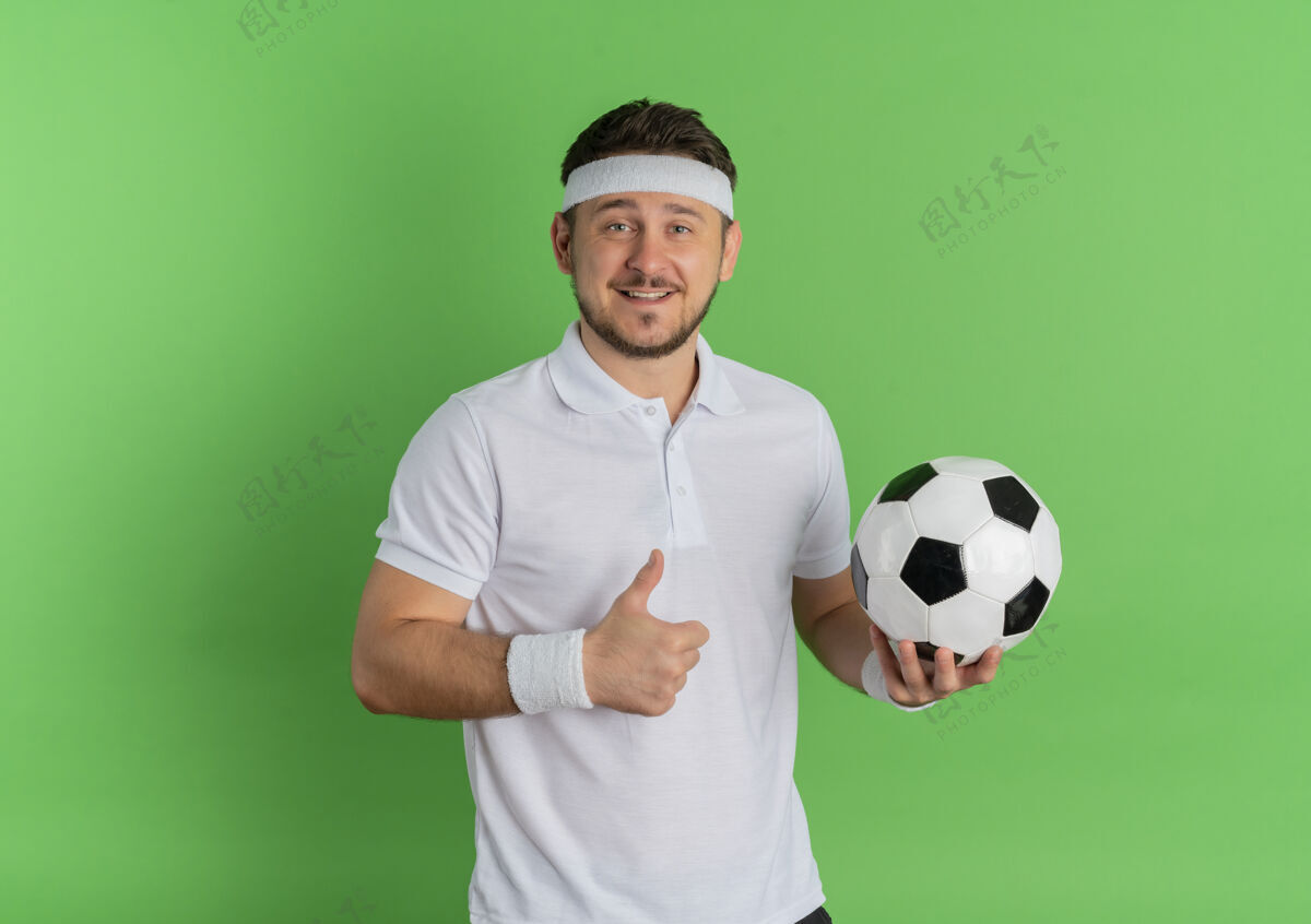微笑身穿白衬衫 头箍 手持足球 微笑着 竖起大拇指的年轻健身男子站在绿色背景上男士欢呼拇指
