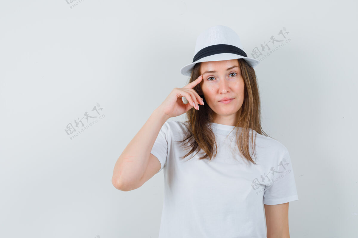 女人穿着白色t恤 戴着帽子的年轻女子用手指在太阳穴上 看起来很懂事成人举行脸