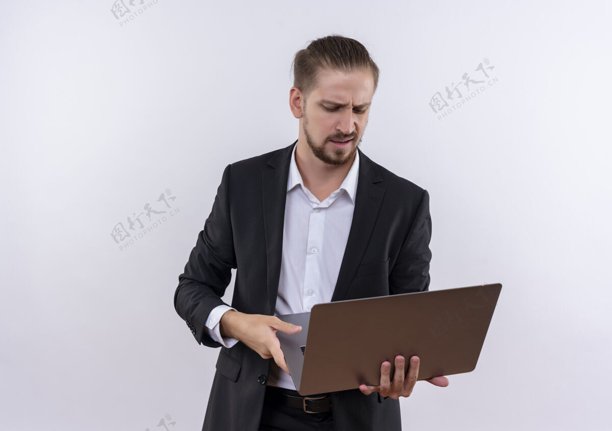 西装穿着西装的帅哥拿着笔记本电脑看着屏幕不高兴地站在白色背景上不高兴穿拿着