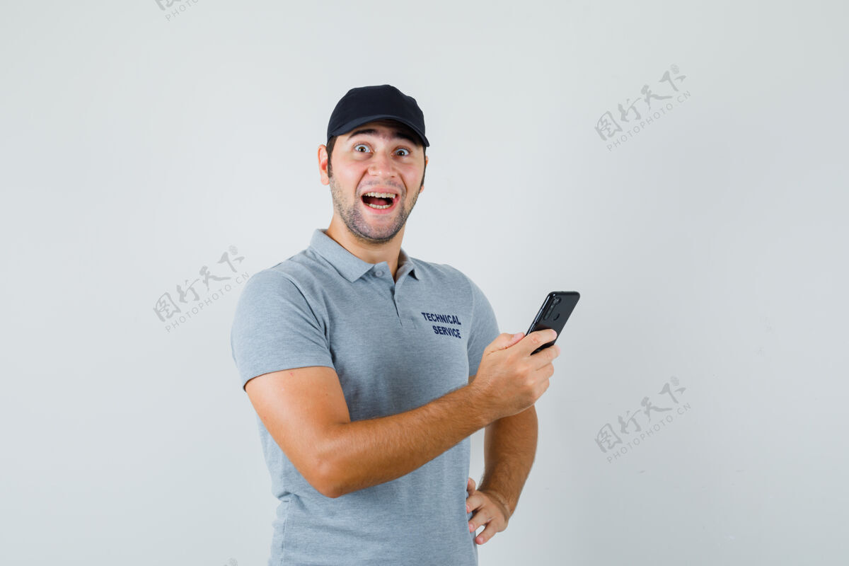 工业年轻的技术员在看手机上的信息 微笑着把他的手放在腰上 穿着灰色制服 看上去很惊讶持有技术工程师