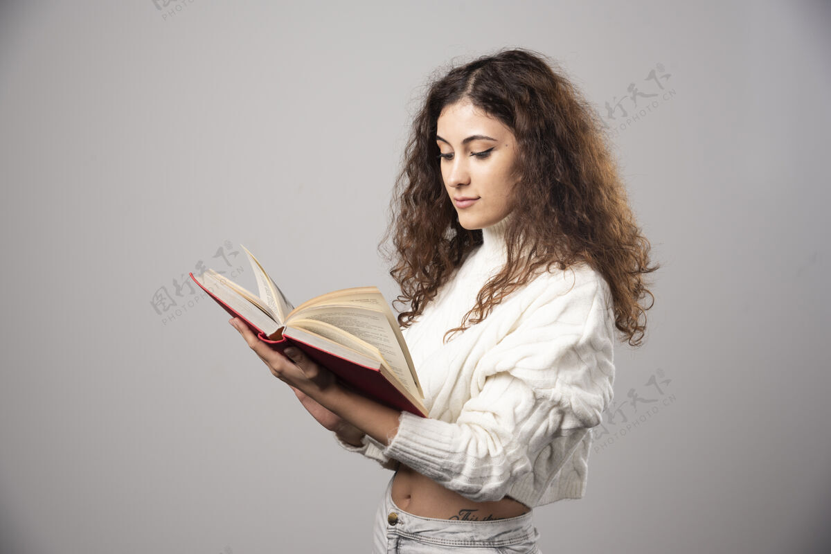 肖像年轻女子在灰色的墙上读着一本红色的书高质量的照片女孩女士人