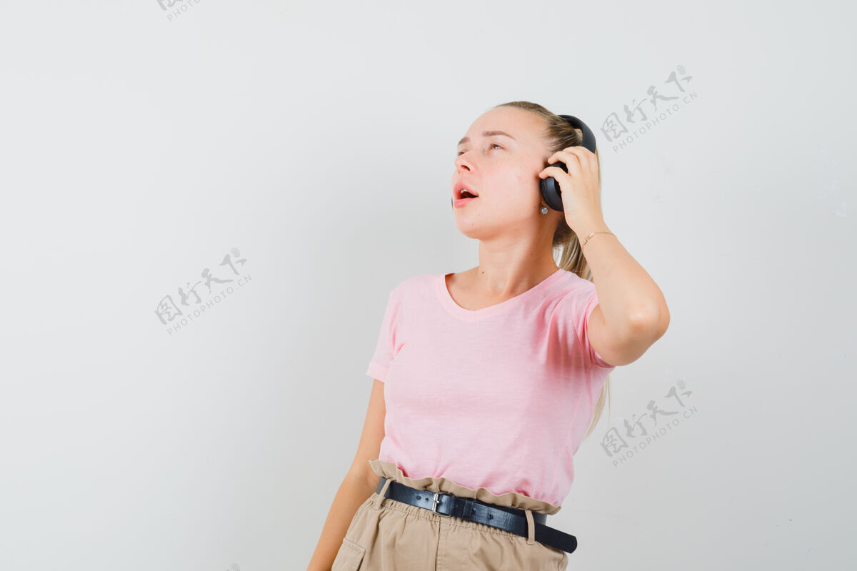 时尚穿着t恤 裤子 戴着耳机听音乐 看起来很高兴的金发女孩 前视图女性时尚音乐