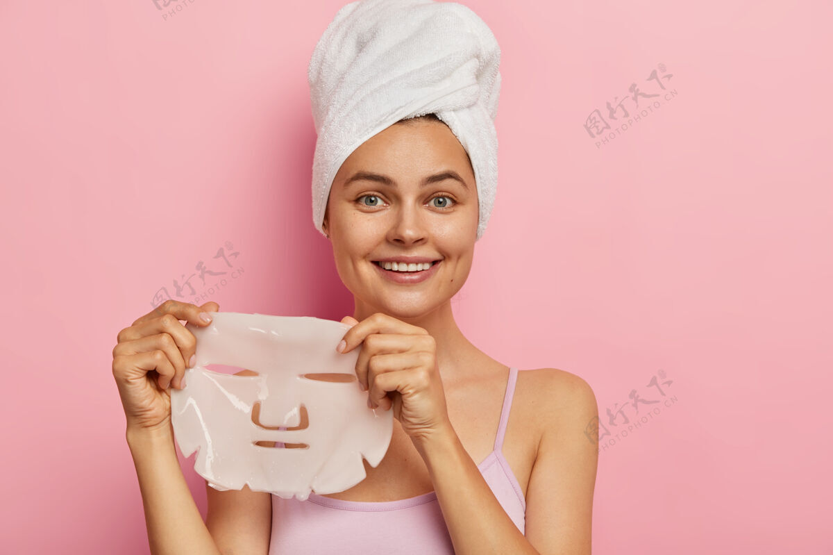 满意肤色治疗理念年轻漂亮的女人拿着凝胶面膜 表情开朗 洗澡后头戴毛巾 穿着休闲装娇生惯养治疗牙齿