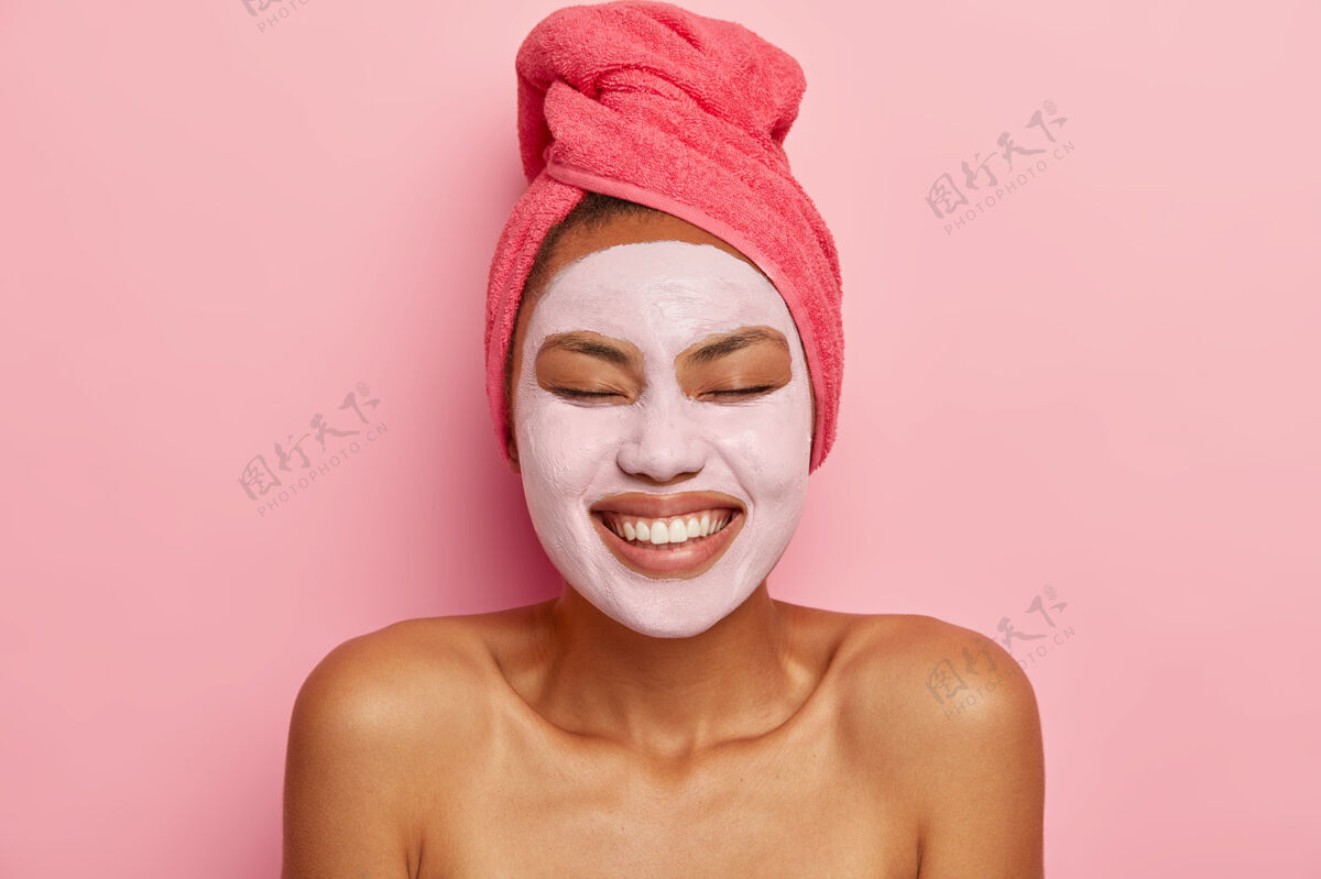 清洁容光焕发的黑皮肤女人头像脸上涂泥面膜 光着肩膀站着 有美容程序 闭着眼睛治疗面霜涂抹