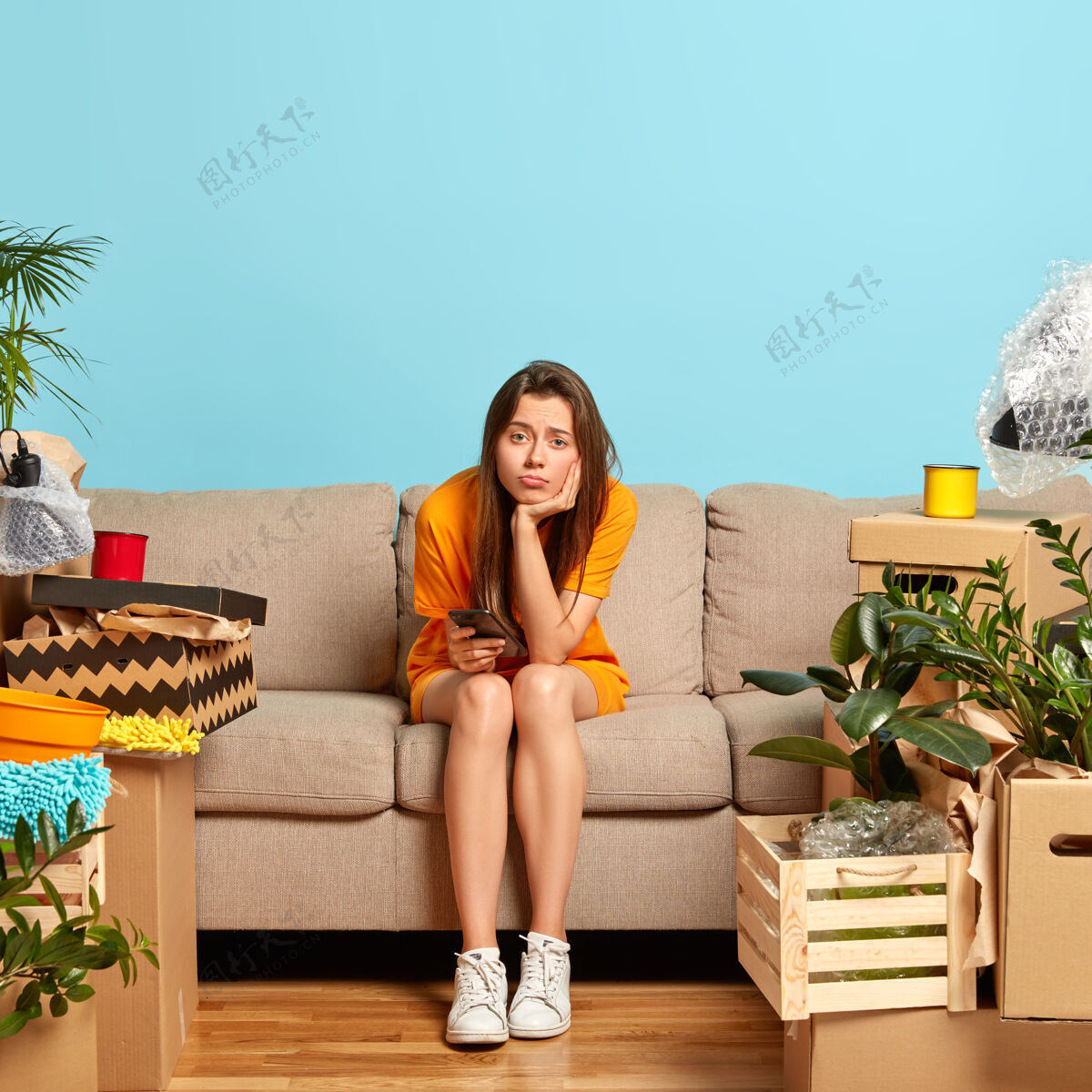 手机不满意的欧洲女人的形象独自坐在客厅的沙发上 感到孤独和沮丧 拿着现代化的手机 搬迁后被纸箱包围 有很多工作要做打开包装沮丧垂直