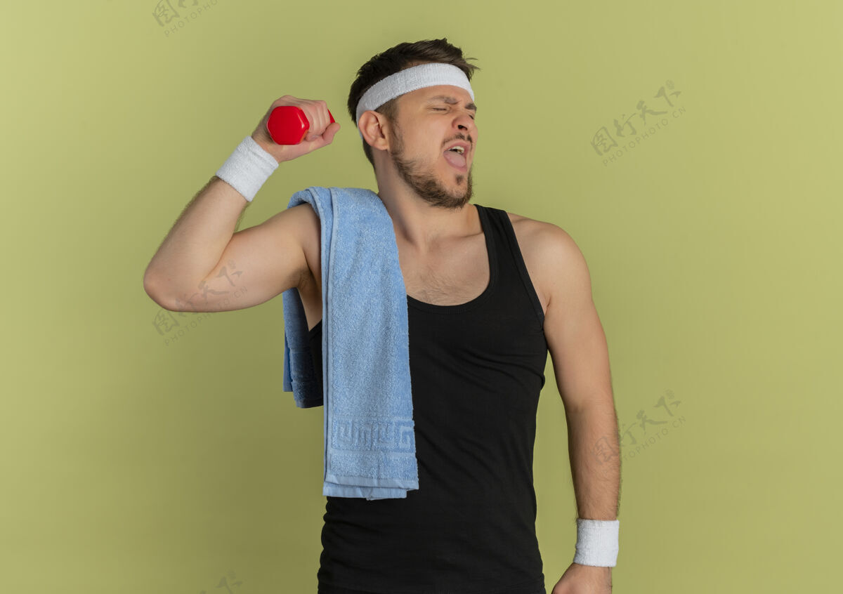 肩膀戴着头带 肩上扛着毛巾 站在橄榄色背景下 一副自信而紧张的哑铃模样 年轻的健身男子在锻炼信心毛巾看