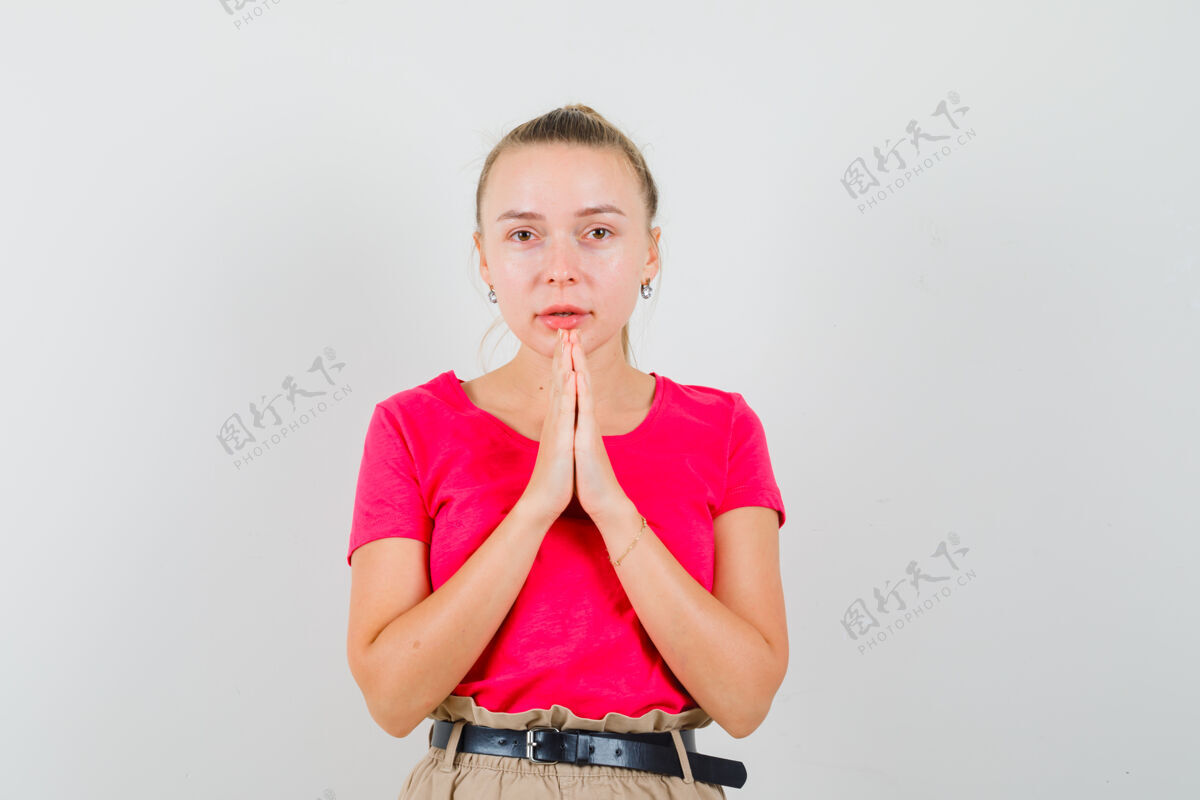 欧洲金发女士手牵手祈祷的姿势在粉红色的t恤 裤子和期待前视图手势女人时尚
