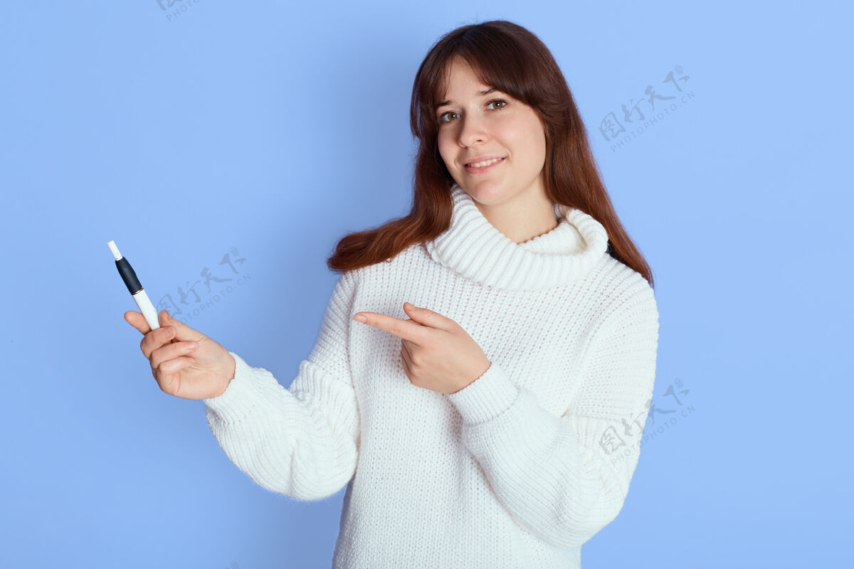 云年轻漂亮的黑发女人用食指指着她的抽电子烟 手指在蓝色的上方 微笑着 可爱的女孩抽着烟 穿着随意蒸汽女性积极