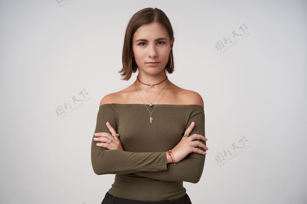 衣服年轻迷人的黑发女士 留着短发 双手交叉 严肃地看着前面 穿着橄榄色上衣站在白色的墙上自然拍摄发型