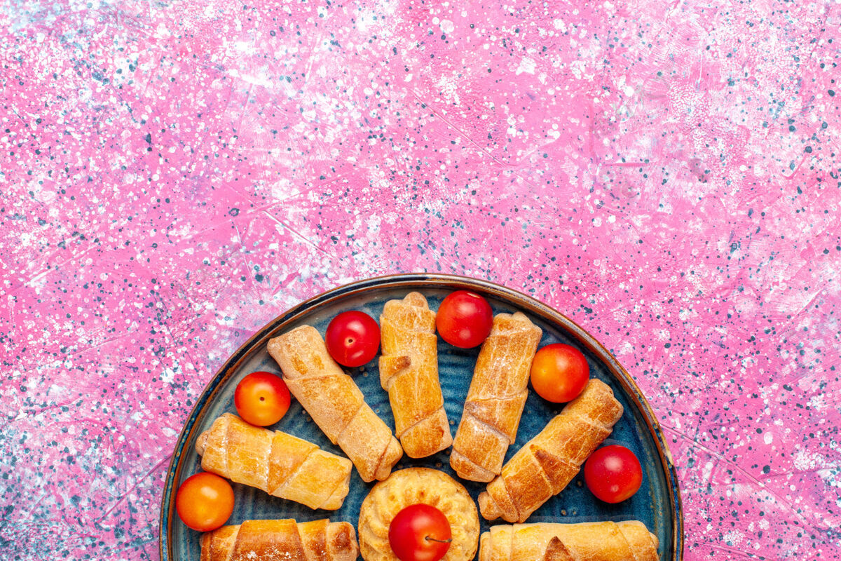 烘焙顶视图甜美美味的百吉饼烤糕点内托盘与李子在粉红色的办公桌上百吉饼饼干午餐