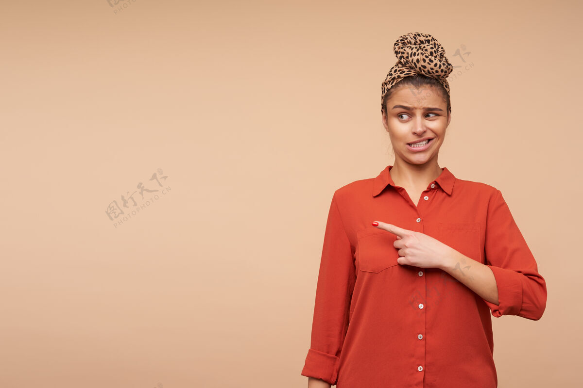 发型迷惑不解的棕色头发的年轻女人 带着自然的妆容 一边扭着嘴 一边用食指困惑地站在一边 站在米色的墙上头发年轻复制空间