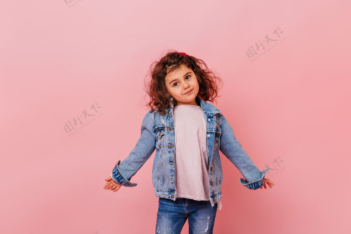 牛仔夹克有趣的小女孩在牛仔夹克看着别处摄影棚拍摄迷人的学龄前儿童孤立在粉红色的背景游戏学龄前儿童女